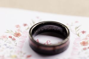 Gold wedding rings are displayed against a white textured background with pink floral accents.