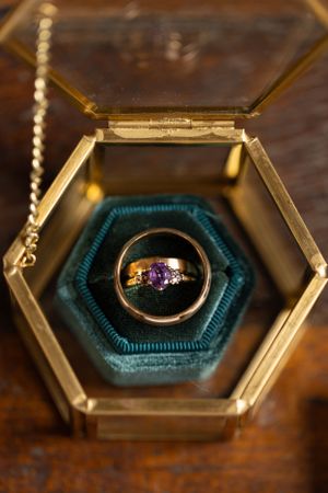 Vintage-style hexagonal ring box with colorful gemstone ring on teal velvet cushion.
