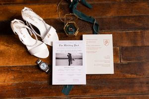 Wedding details flatlay with white shoes, invitations and decorative elements on wooden surface.