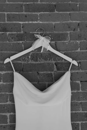 A white wedding dress hanging on a personalized hanger against a brick wall.