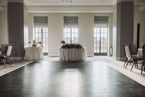 Elegant event space with round table draped in white linens, tall windows, and dark columns in a minimalist setting.