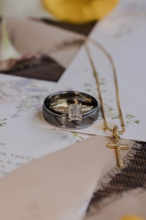 Wedding rings and gold necklace arranged on textured white paper with elegant wedding invitation details.