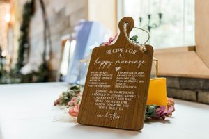 Wooden cutting board engraved with Recipe for a Happy Marriage displayed as wedding decor on a white table.