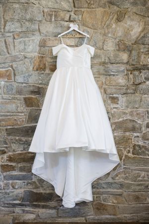 White wedding dress hanging on stone wall with dramatic train.
