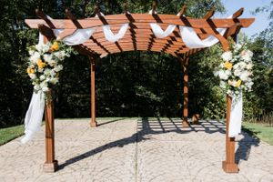 Wooden wedding pergola decorated with white flowers and fabric draping on a stone patio.