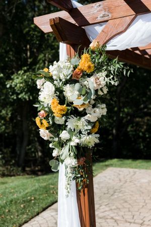Floral arrangement with white and yellow flowers adorning a wooden pergola post.