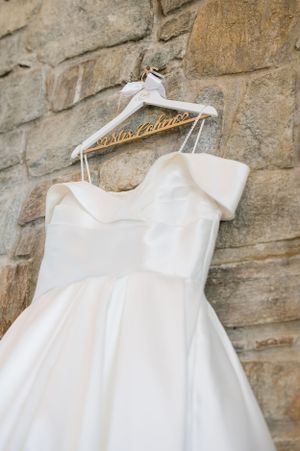 Classic white wedding dress hanging on personalized hanger against stone wall.