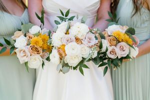 Wedding bouquets featuring white roses, yellow flowers and greenery against mint green dresses.
