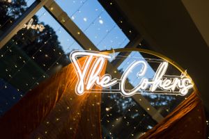 Illuminated neon sign reading 'The Cohen' on reflective surface at night.