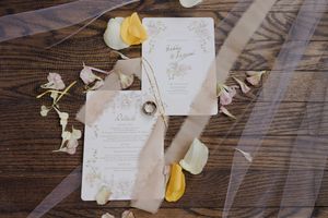 Wedding invitation cards with citrus slices and floral details arranged on rustic wooden surface with rings.
