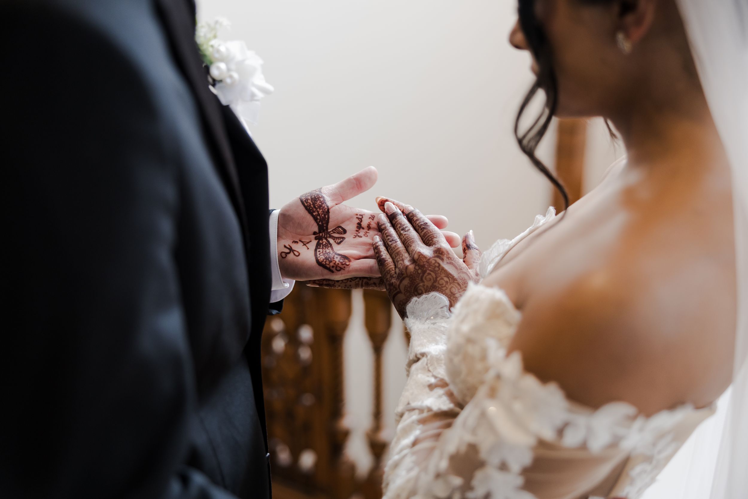 Bride and groom exchanging rings during wedding ceremony, close-up of hands in elegant lace gown and black suit.