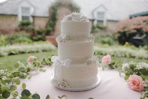Elegant white wedding cake decorated with delicate pearl details and fresh roses sits on decorated reception table.