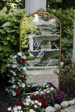 Series of ornate gold-framed mirror signs amongst red and white flowers in a garden setting.