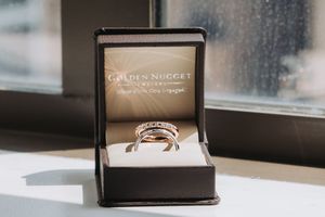 A shiny diamond engagement ring sits in an open black Golden Nugget jewelry box near a window.