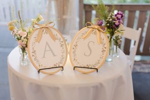 Two gold engagement rings sit on blush-colored paper hearts decorated with delicate floral arrangements and greenery.