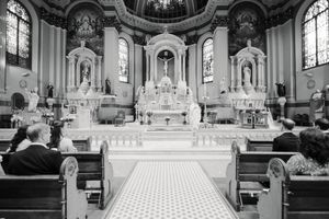 Elegant Catholic church interior with ornate altar, white columns, and worship service in progress.