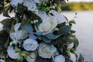 White roses and eucalyptus leaves create an elegant floral arrangement against a waterfront backdrop.