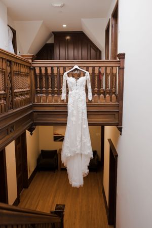 Lace wedding dress with long sleeves hanging from wooden balcony railing in a rustic interior staircase.