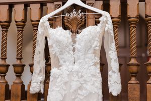 Close-up of lace long-sleeve wedding dress on a custom Mrs. hanger draped over a wooden banister.