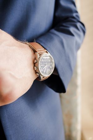 Close-up view of a brown leather watch strap with a minimalist analog timepiece against a navy blue sleeve.