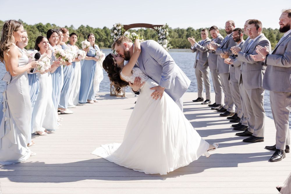 Wedding guests in gray suits dance with brides in white dresses during an outdoor celebration.