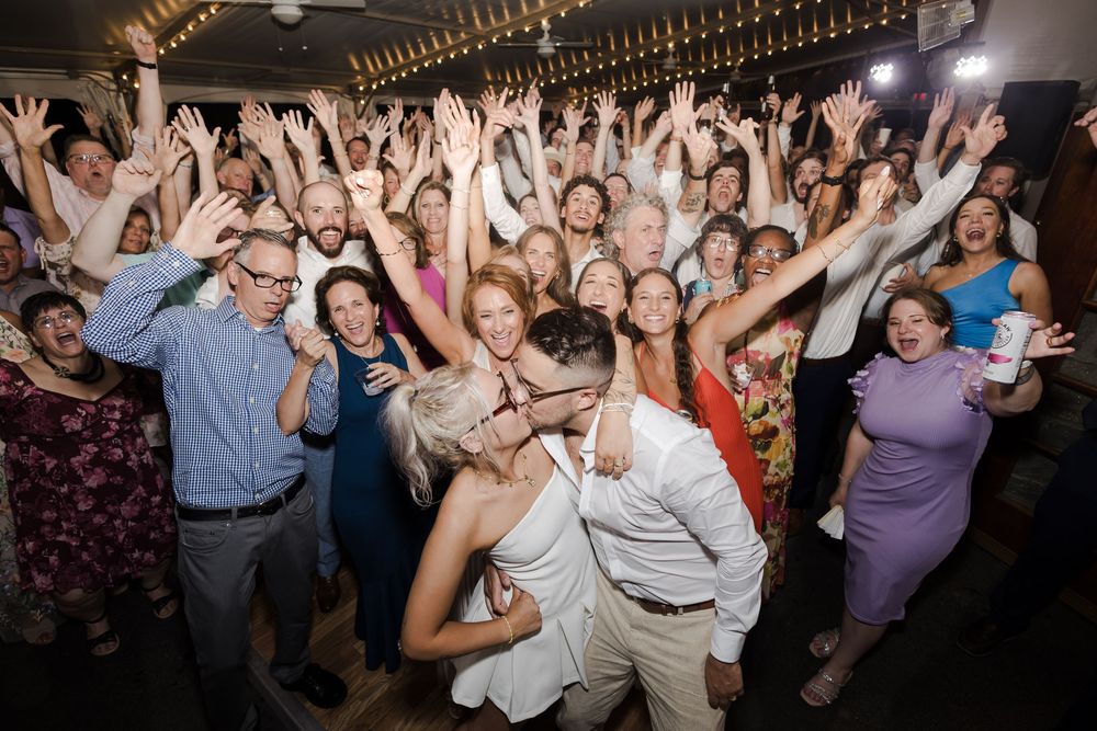 People dancing and celebrating with raised arms on a crowded dance floor at an energetic party.