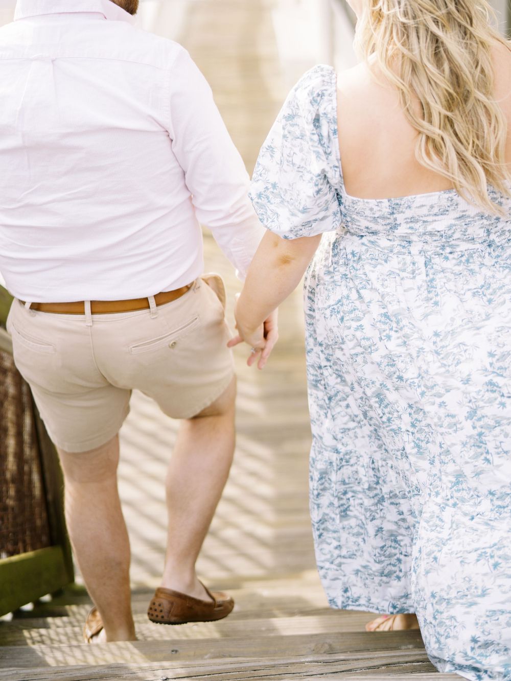 A couple walking hand in hand wearing coordinated summer outfits on a wooden walkway.