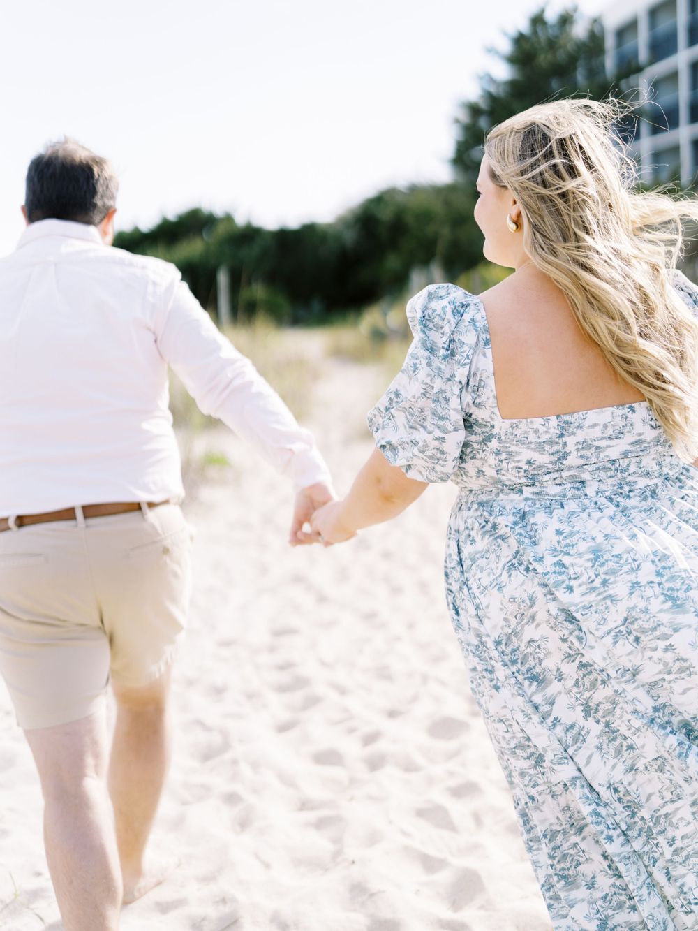 A couple holding hands while walking along a sandy beach path on a sunny day.