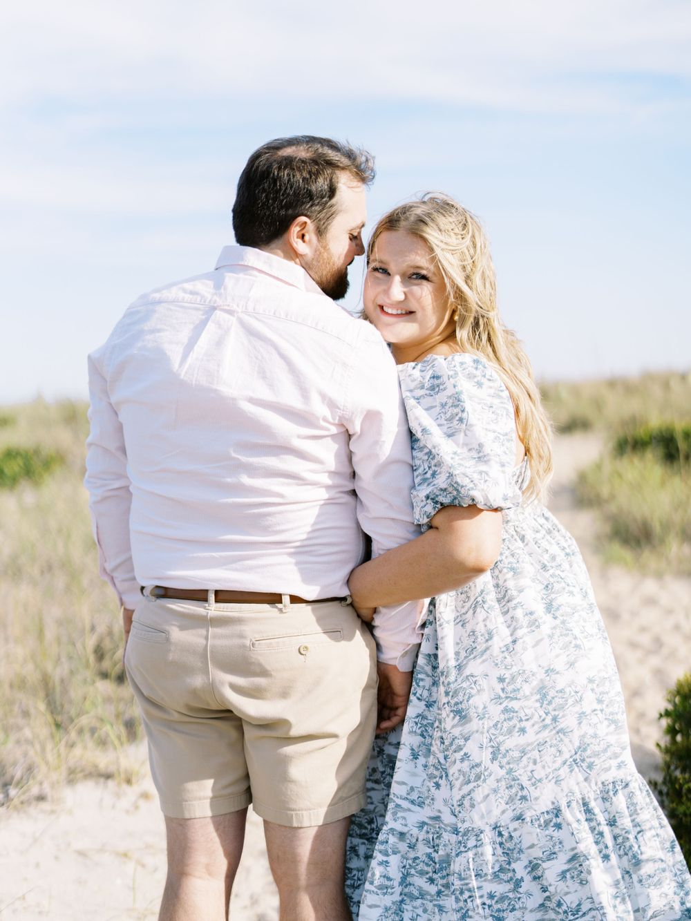 A couple in coordinating outfits sharing an intimate moment on coastal dunes.