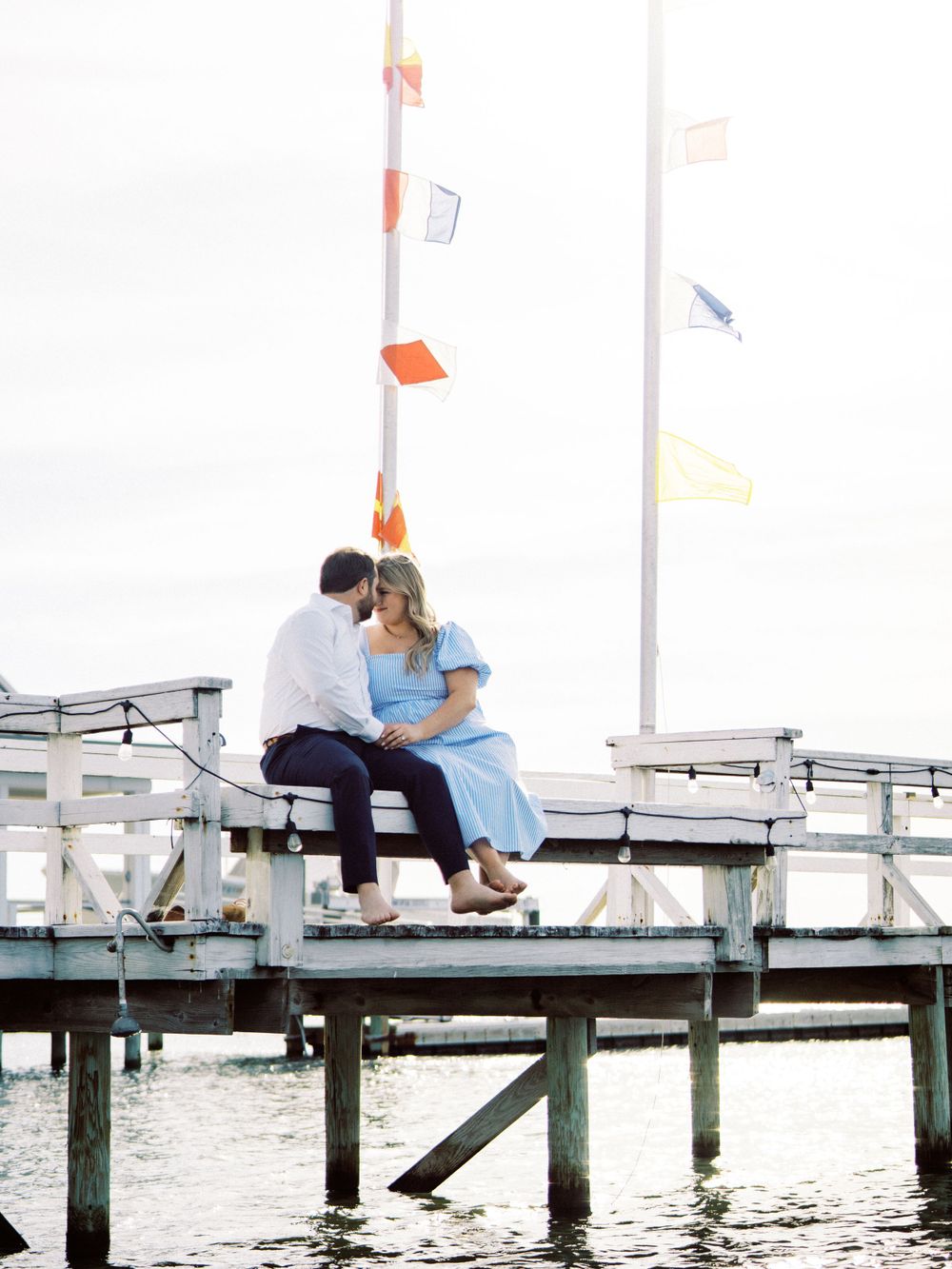 Couple sitting together on a wooden pier with nautical flags waving above.