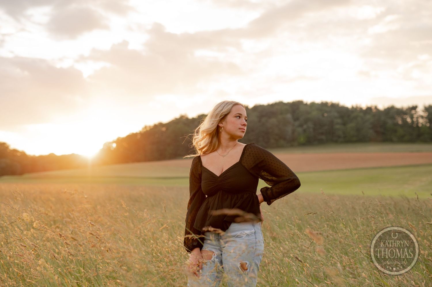 Warm sunset portrait in a grassy field wearing casual distressed denim and black top.