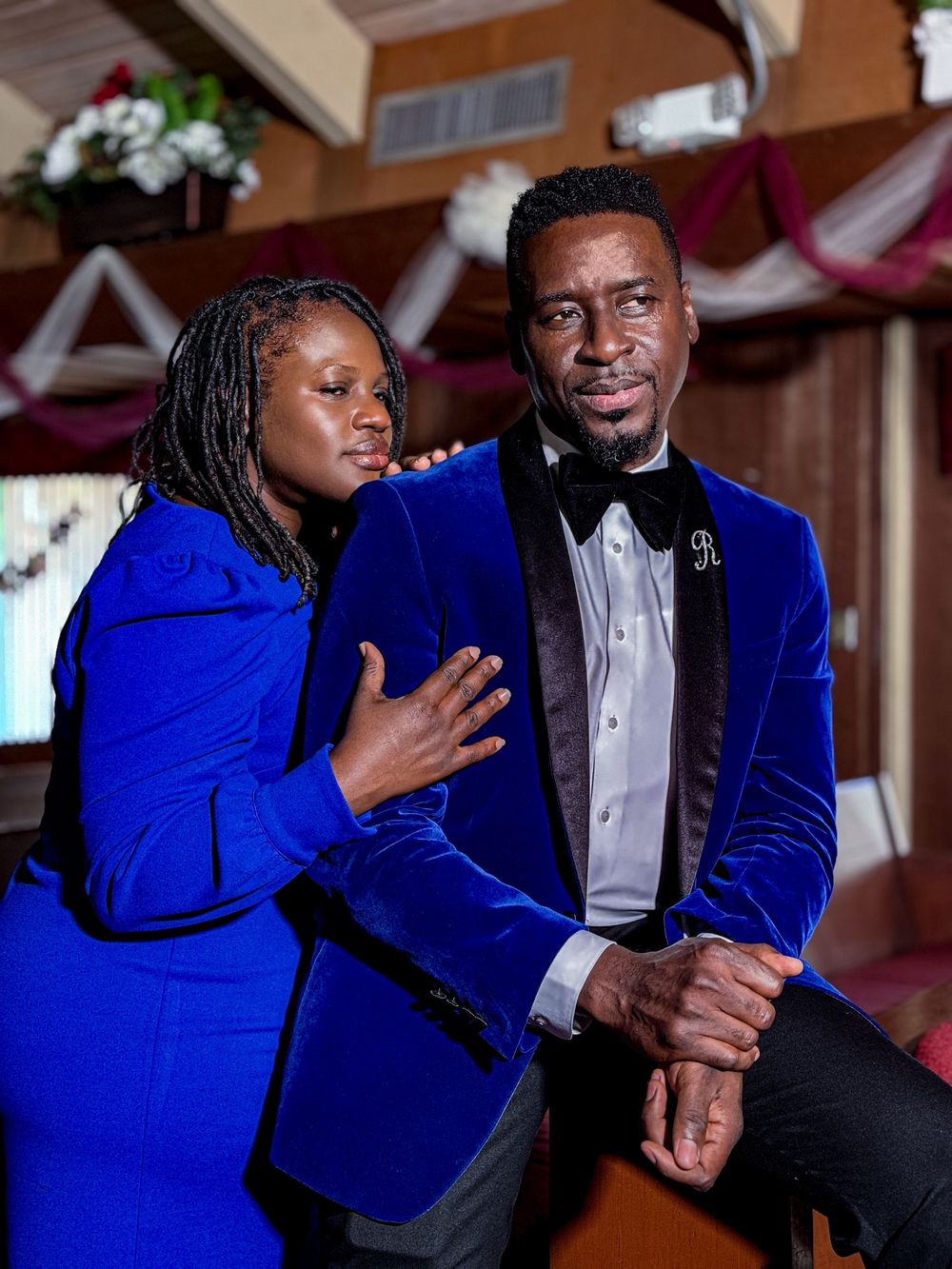 A couple in matching royal blue velvet formal wear pose together at an elegant event venue.