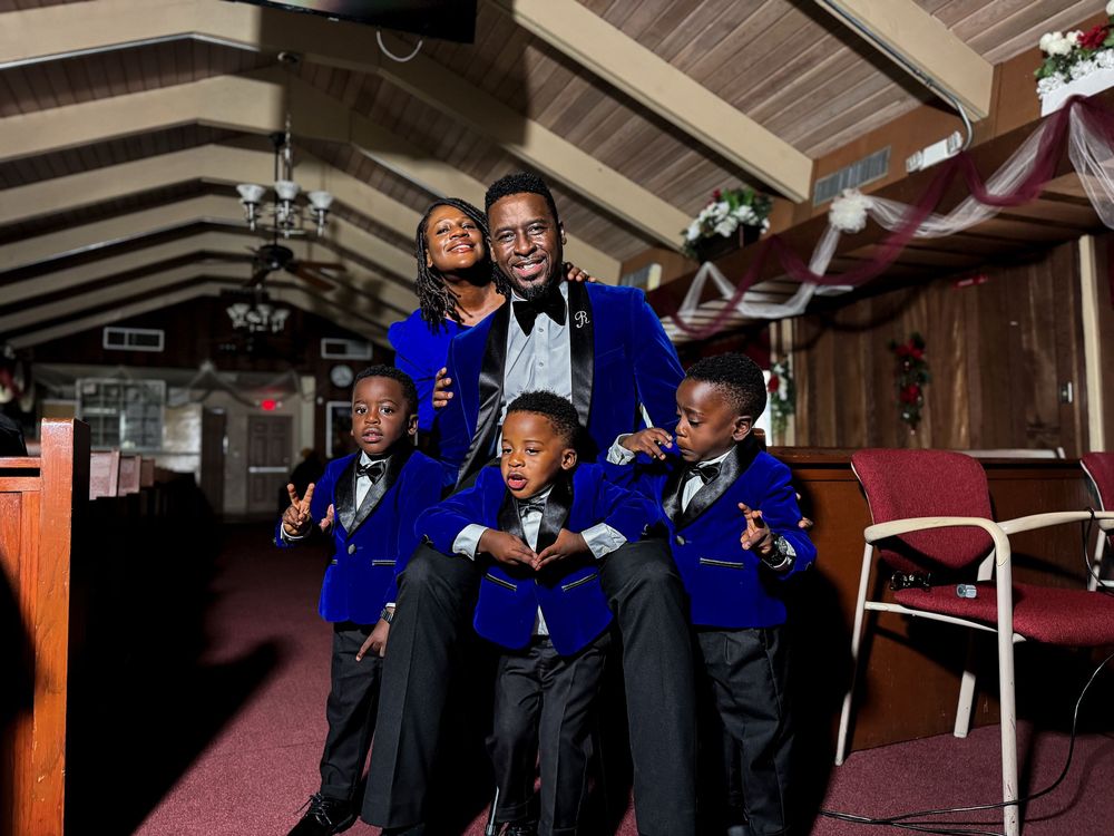 A group in matching royal blue jackets and bow ties pose together in a rustic venue with wooden beams.
