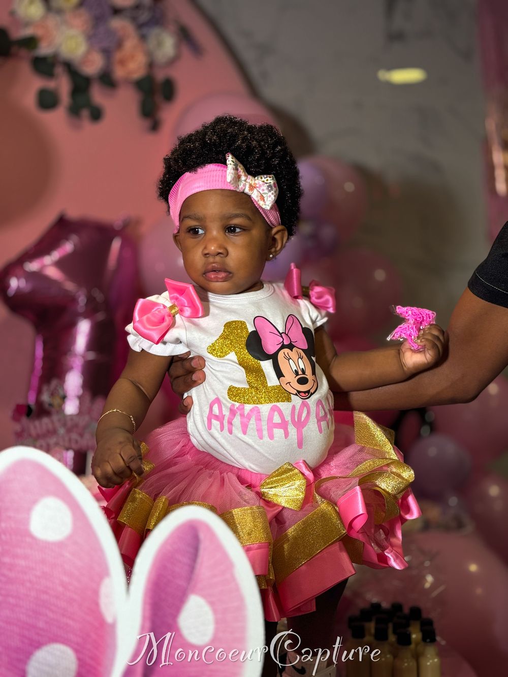 A small child in a pink and gold tutu dress with Minnie Mouse themed outfit celebrating a special occasion.