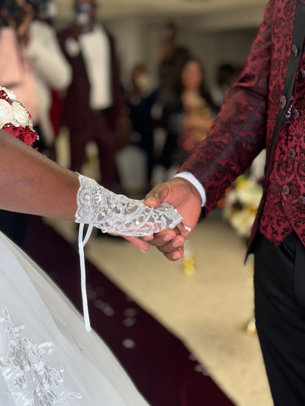 Close-up of hands holding during a wedding ceremony, showing delicate white lace bridal gloves and formal attire.