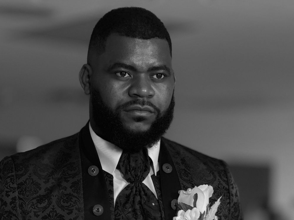 Black and white portrait of person wearing formal suit with boutonniere.