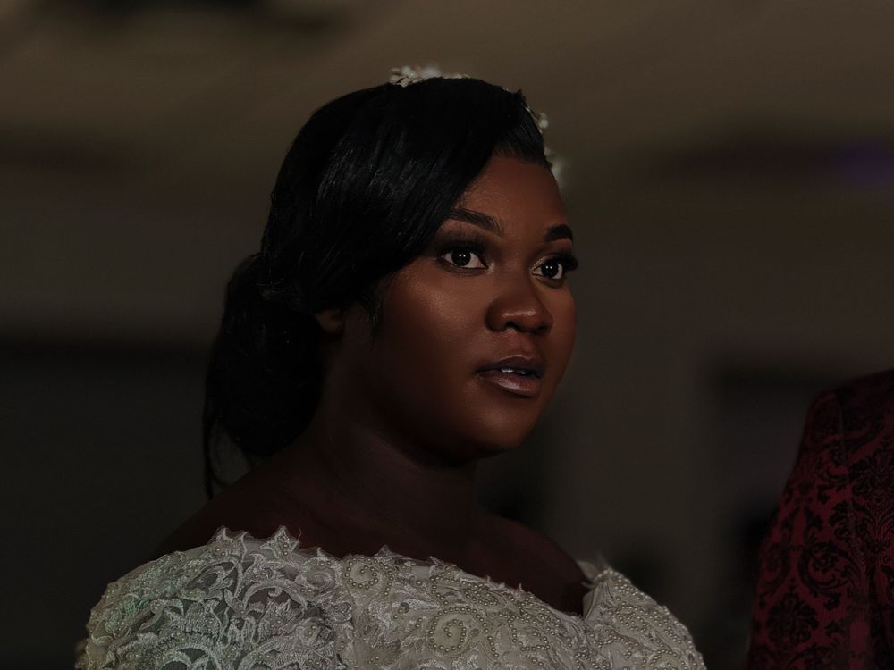 A person in a white lace dress against a dark background gazes off-camera with an expressive look.