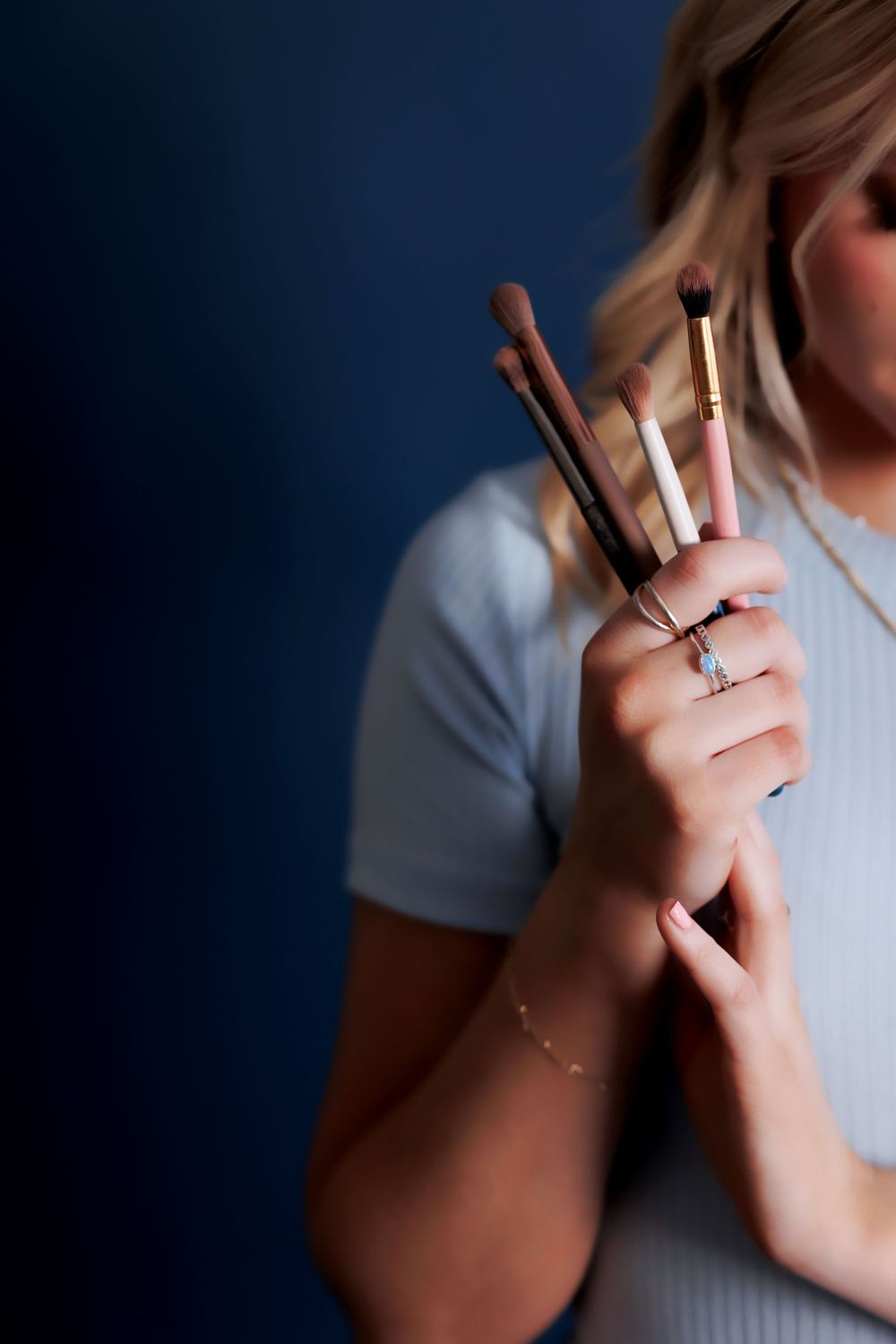 Close-up of hands holding makeup brushes against dark blue background.