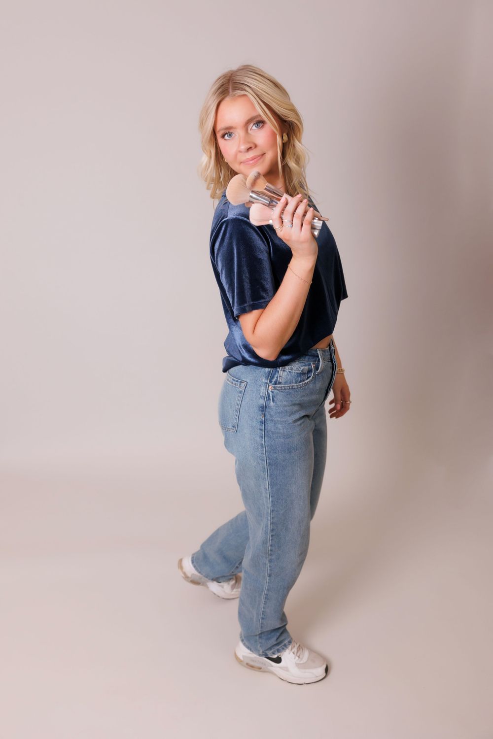 Full body shot of woman in navy top and jeans posing against neutral backdrop.