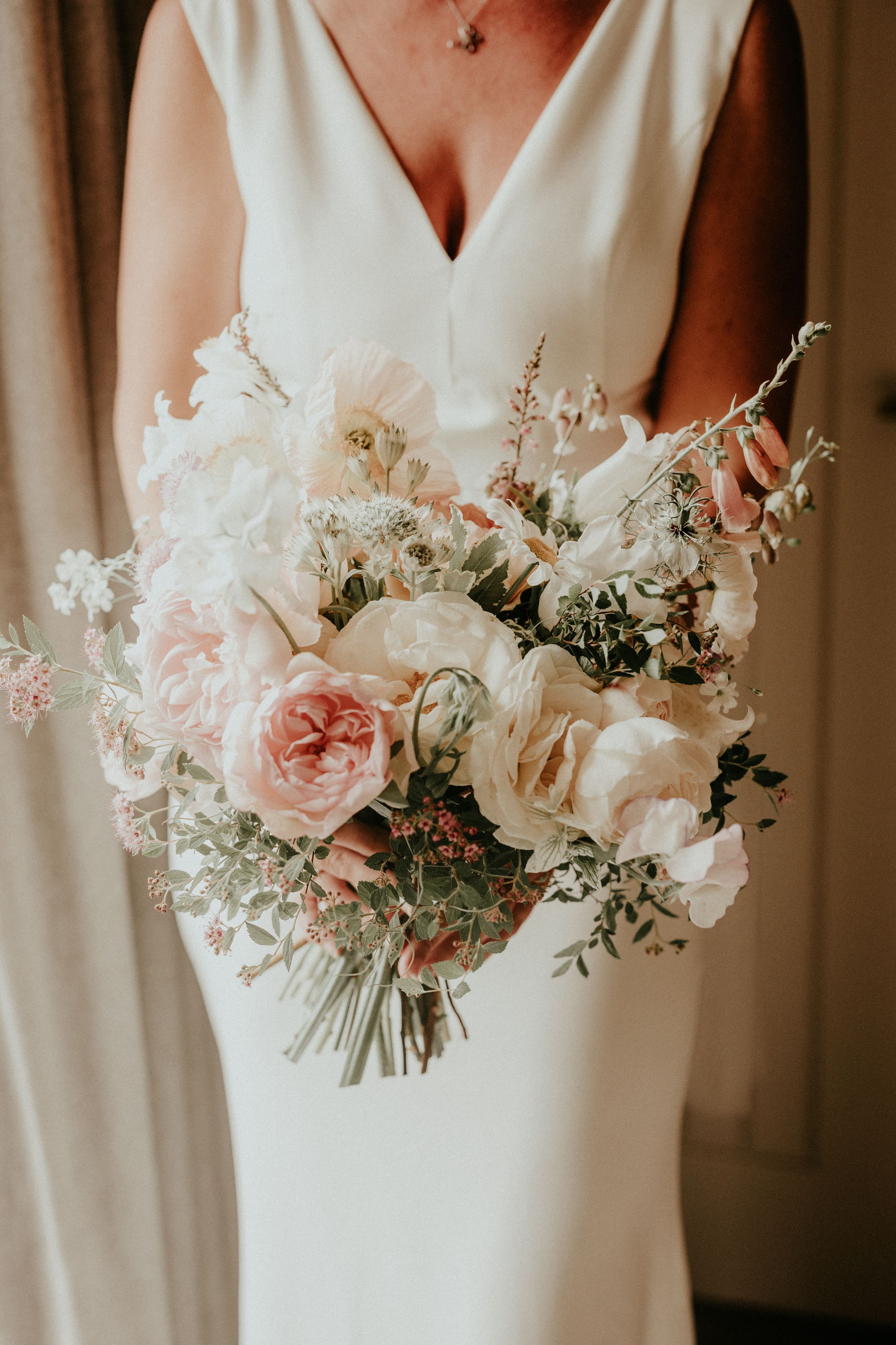 Bride in white gown holding romantic bridal bouquet of blush pink roses, white peonies, and greenery.