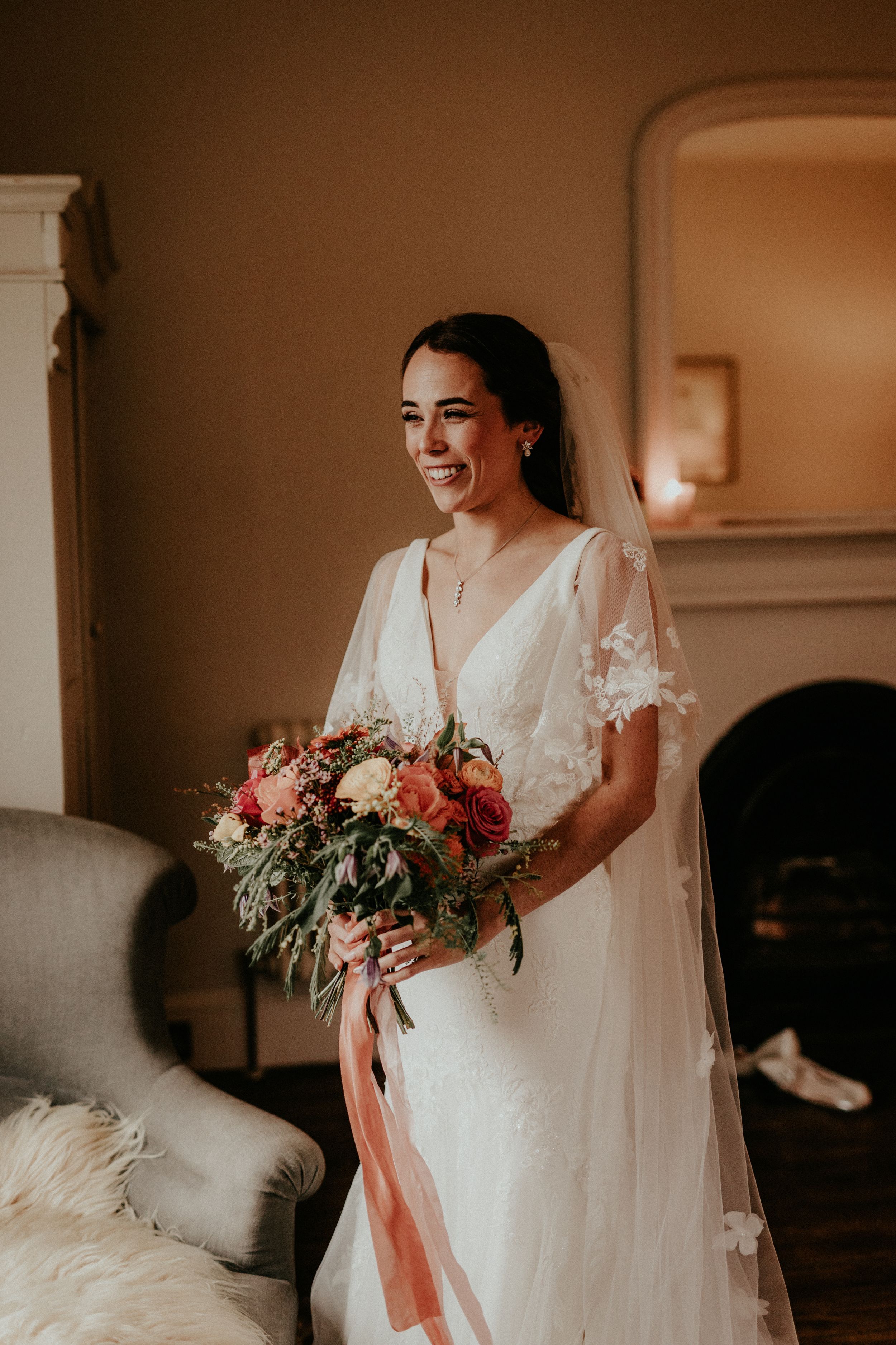 Joyful bride in lace-detailed gown holds vibrant bouquet in elegant indoor setting.