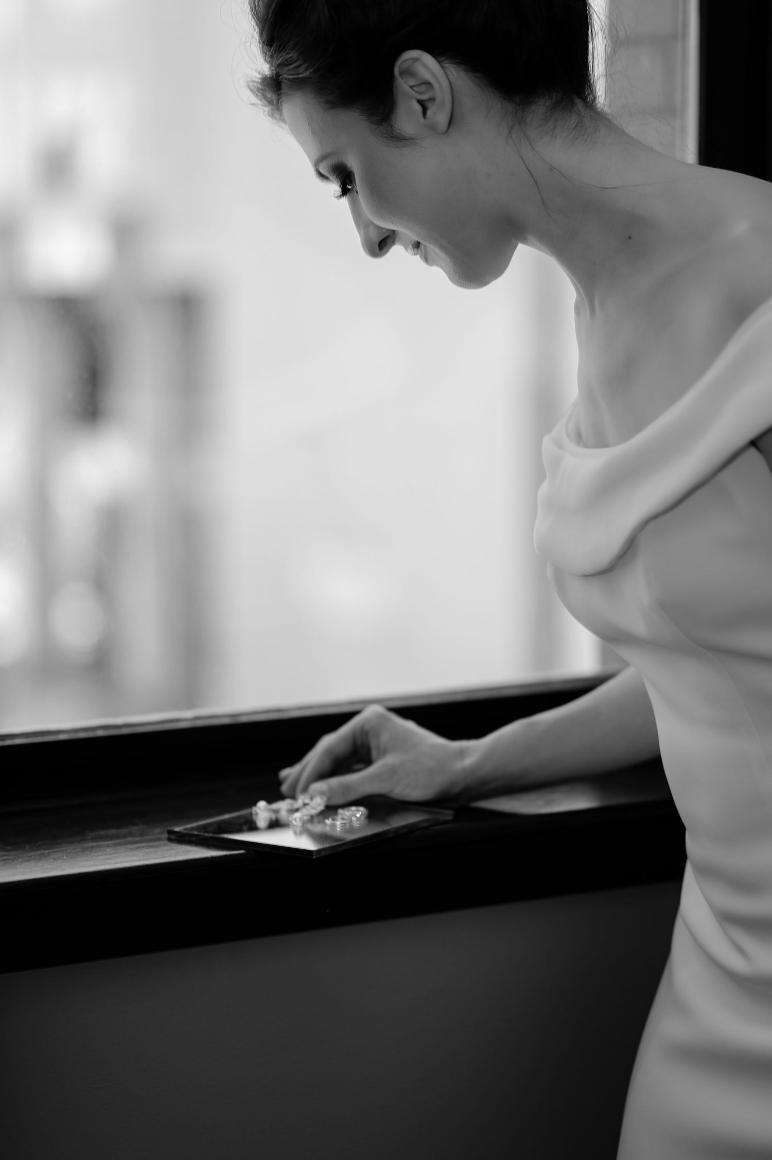 A black and white photo shows someone in a white outfit resting their head on a window ledge.