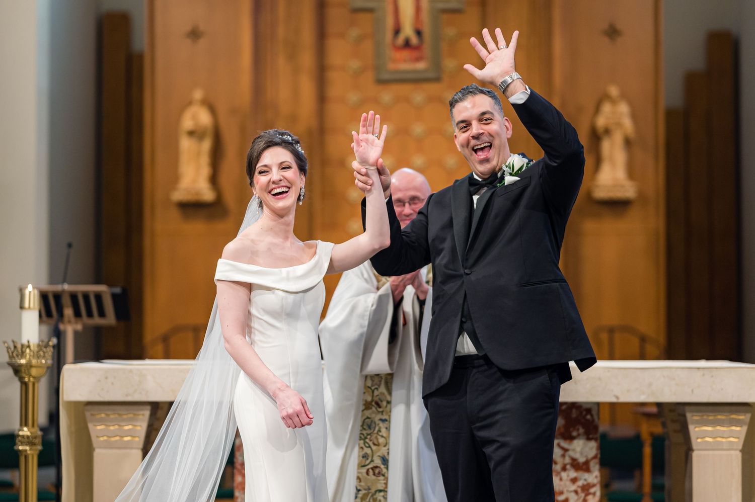 Newlywed couple waves joyfully to guests inside a church's ornate altar area during their wedding ceremony.