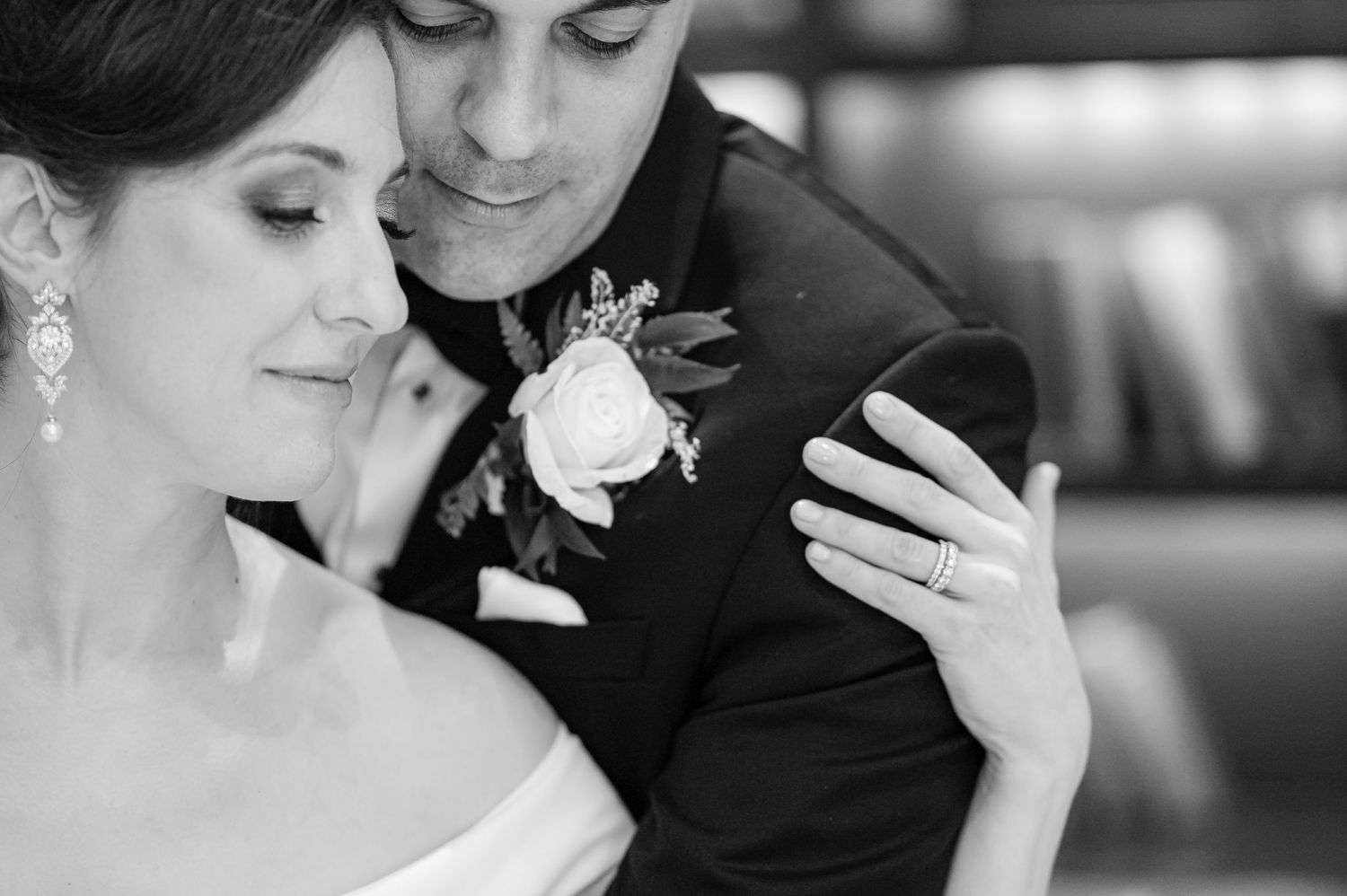 A black and white intimate wedding photo showing a tender embrace between two figures with boutonnieres and formal attire.
