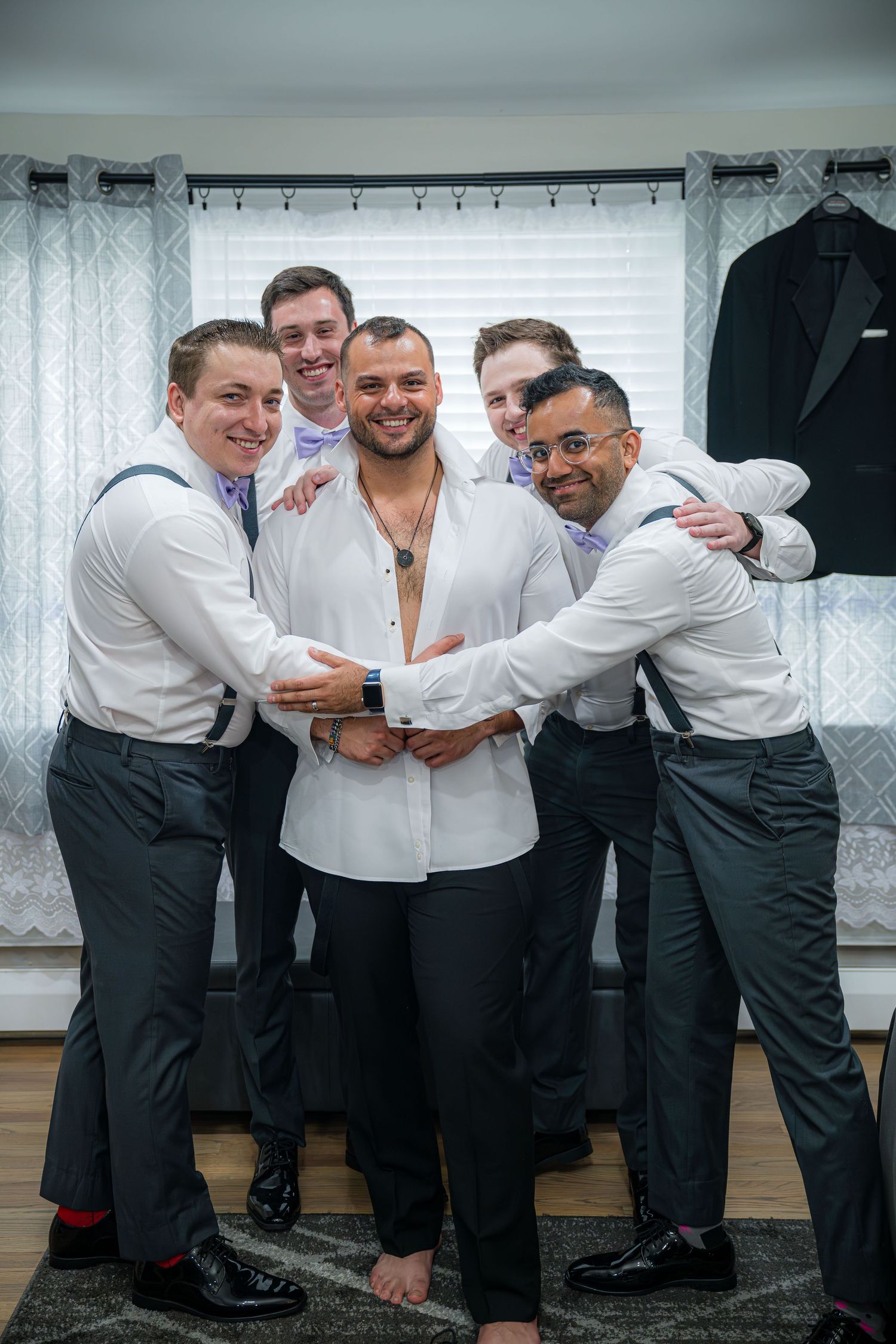 A group of groomsmen in black and white attire share a playful moment while getting ready for a wedding celebration.
