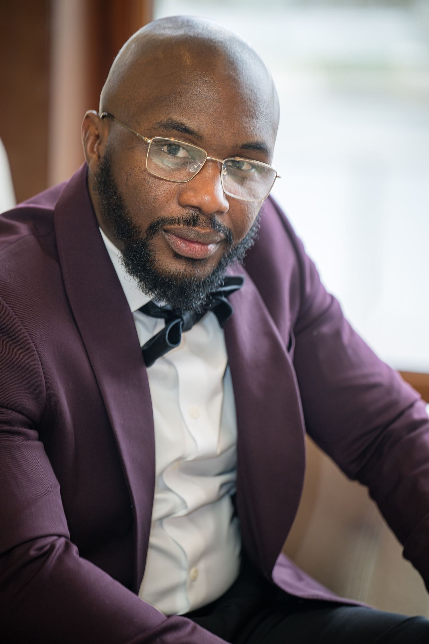 A person wearing glasses and a purple suit jacket smiles warmly while seated in an indoor setting.