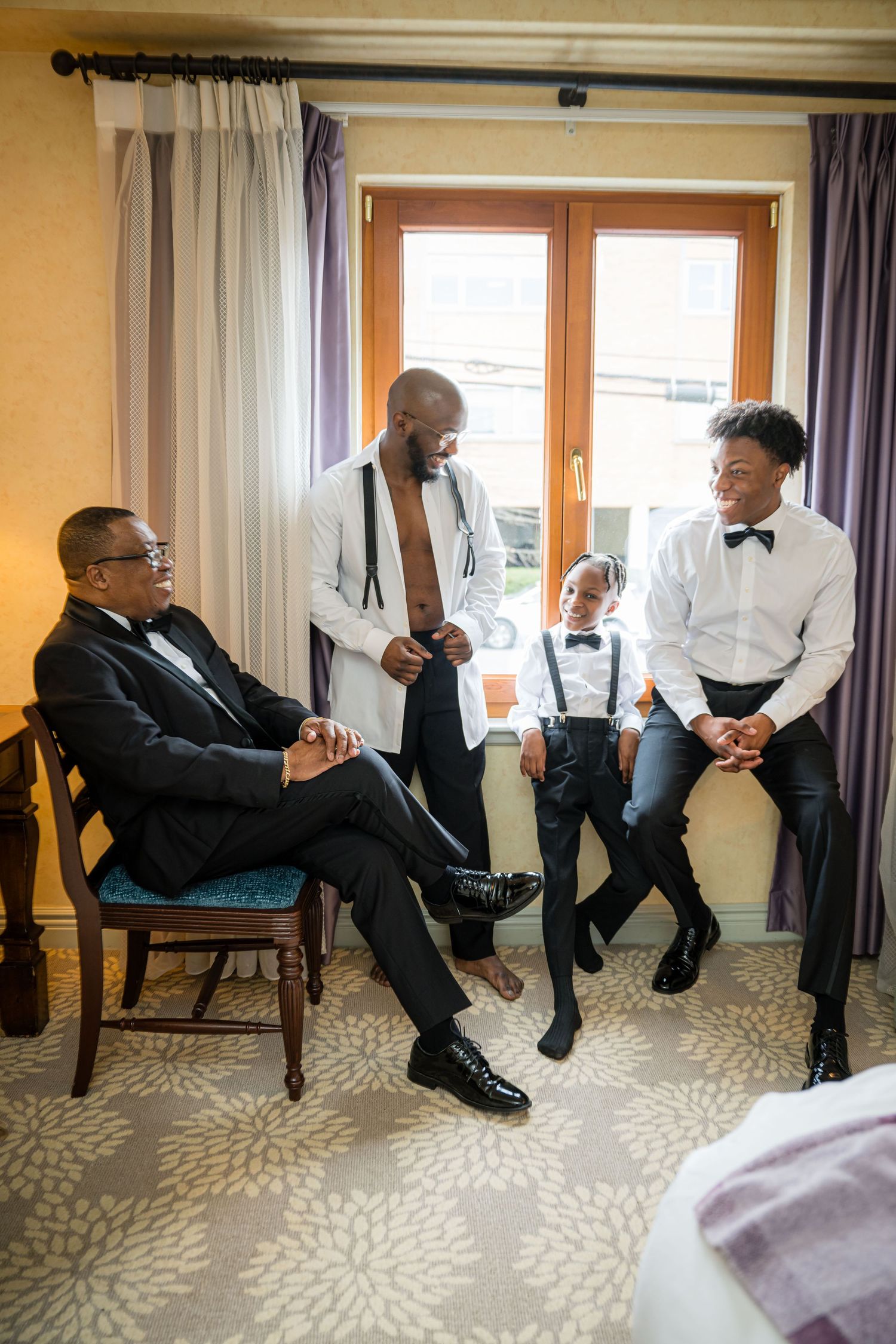 A series of groomsmen in formal attire relaxing and showing off their socks while seated in a row at a wedding venue.