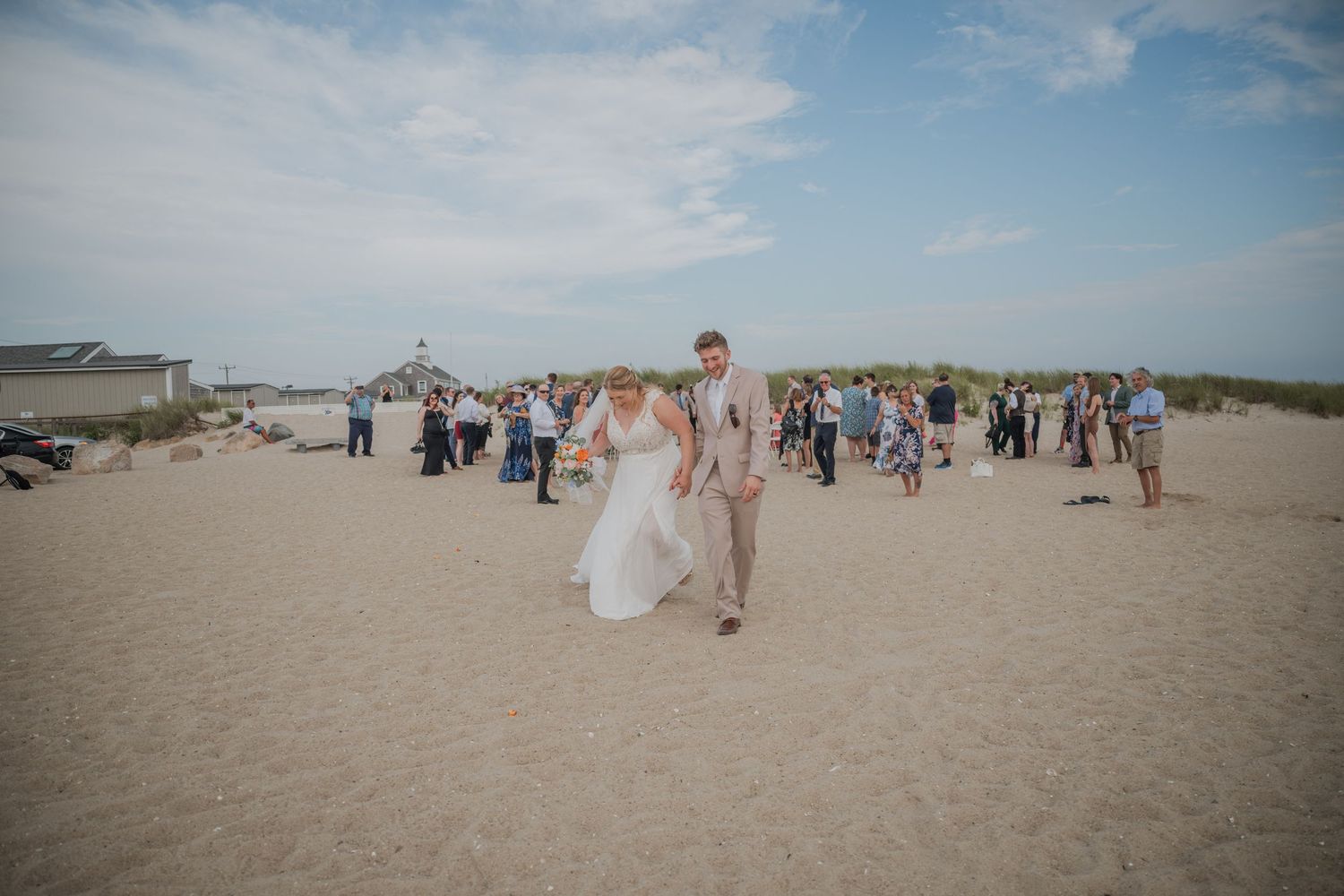 A beach wedding ceremony with guests gathered on sandy shores under blue skies.