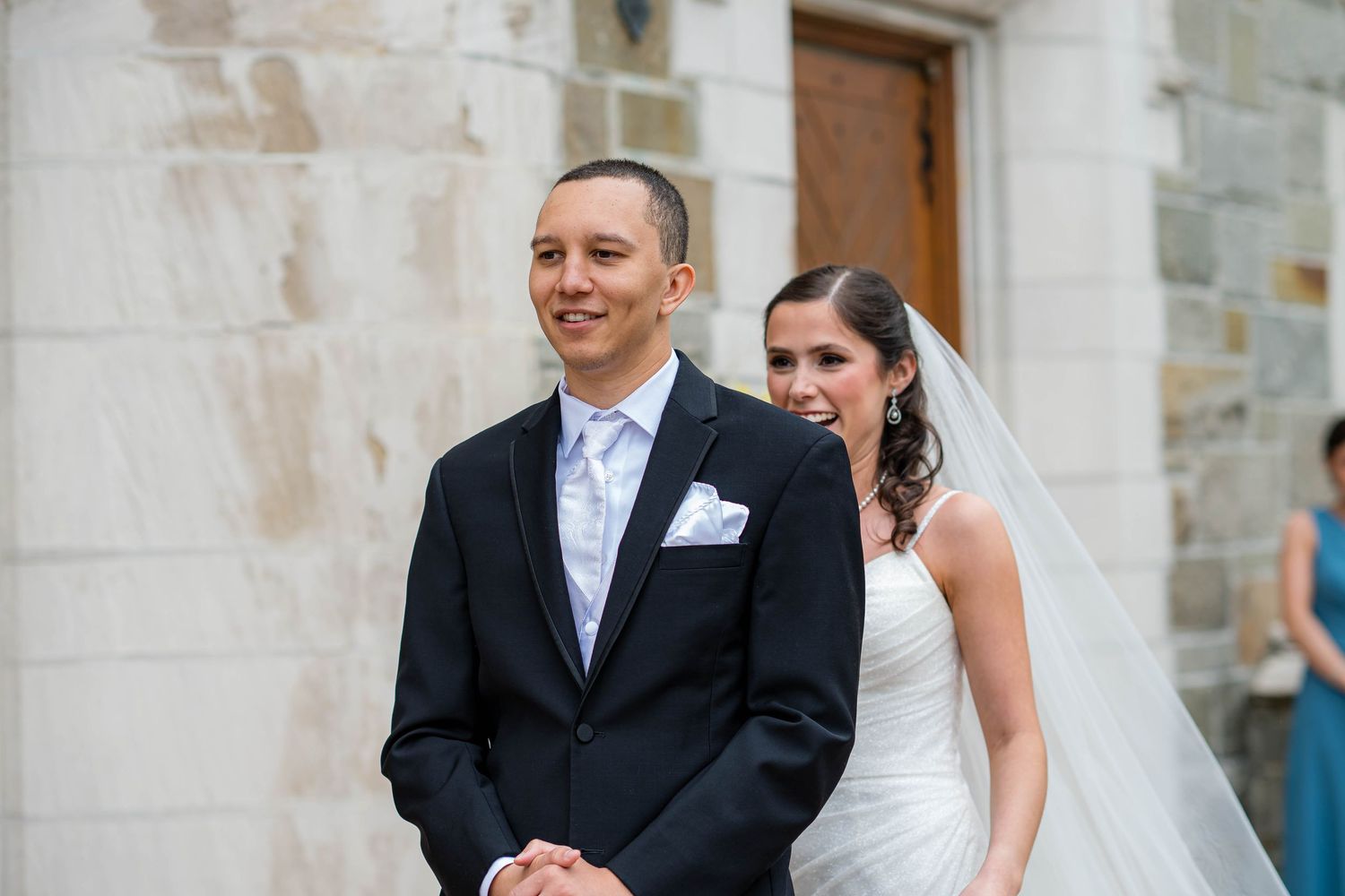 A joyous newly married couple laughs together while walking outdoors near stone columns.