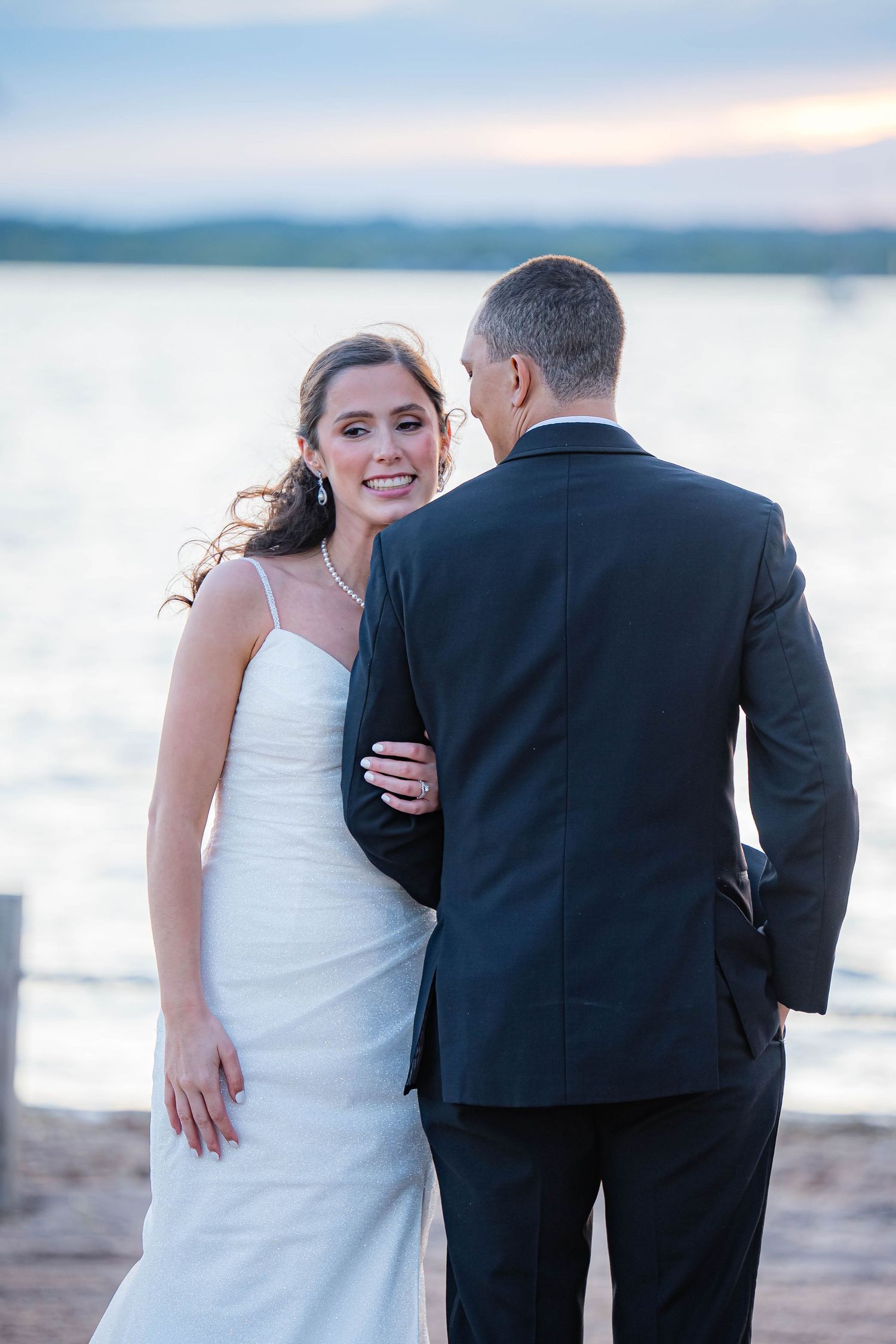 A romantic beach wedding photoshoot at sunset with couple in formal dress embracing by the water.